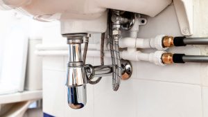 Exposed plumbing pipes and drain fittings underneath a bathroom sink